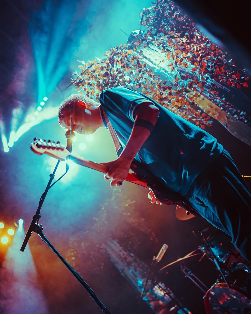 Briston Maroney. A guitarist seen from below leans forward under cyan light and a burst of confetti.