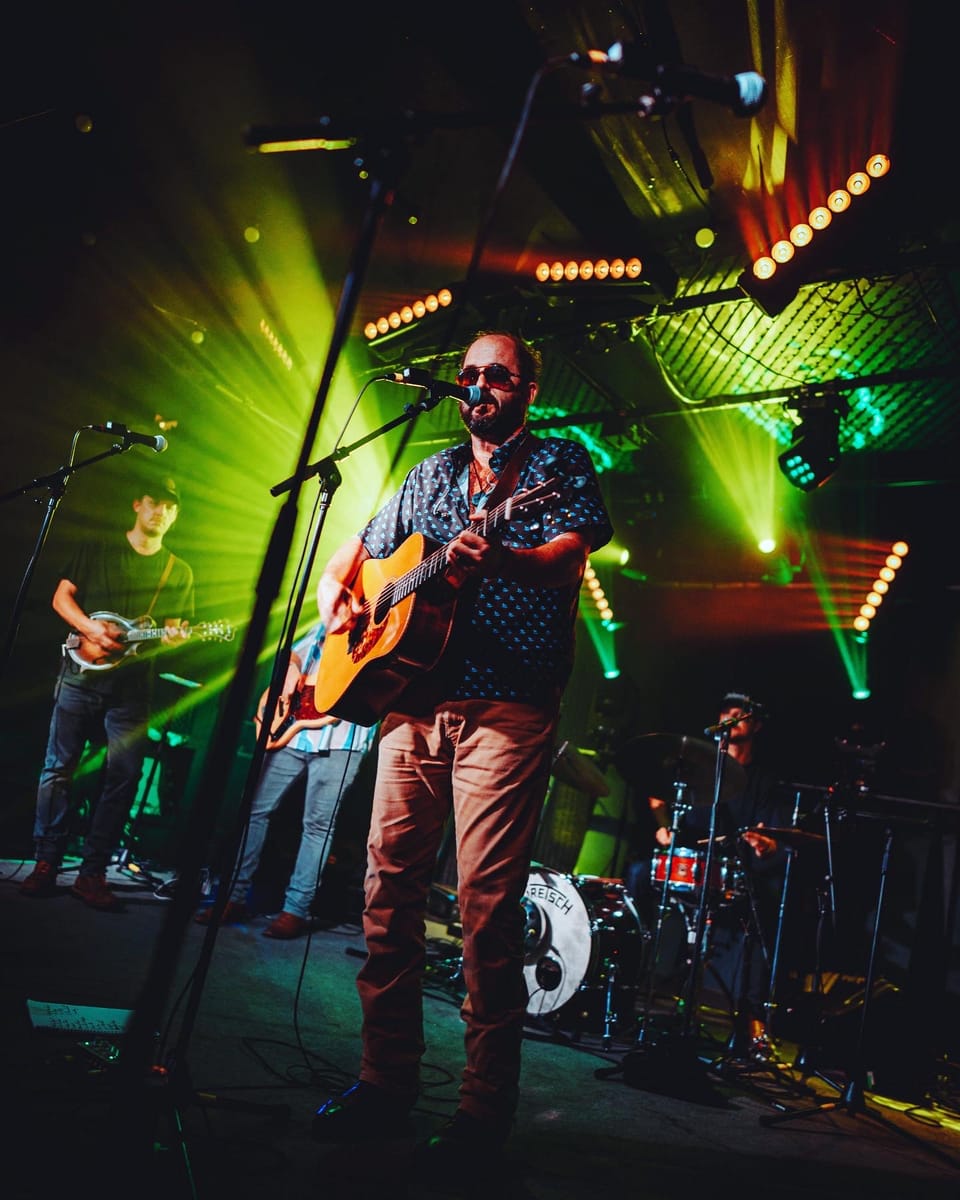 Town Mountain. A singer in sunglasses plays an acoustic guitar against green stage lights.