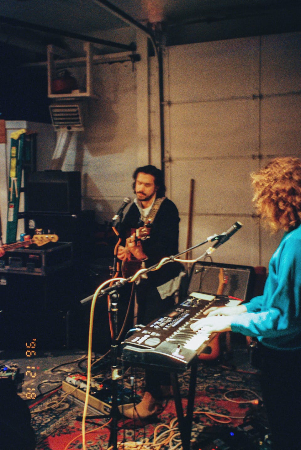 Mo Lowda and the Humble. Two musicians play in a garage-style studio, surrounded by a keyboard and guitars.