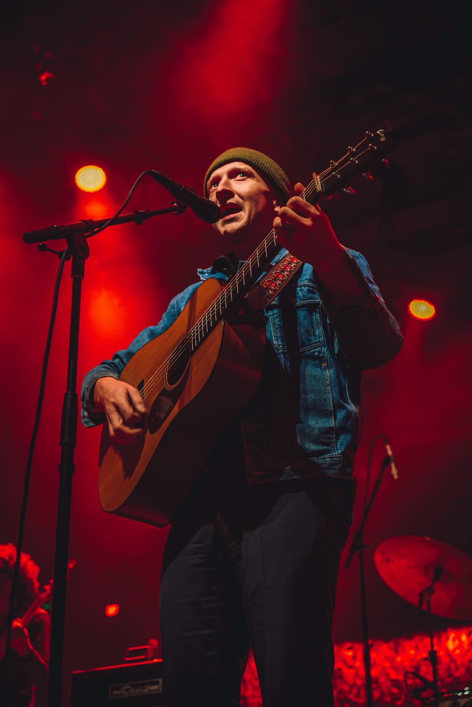 Tyler Childers. A singer in a beanie plays acoustic guitar at a microphone in deep red light.