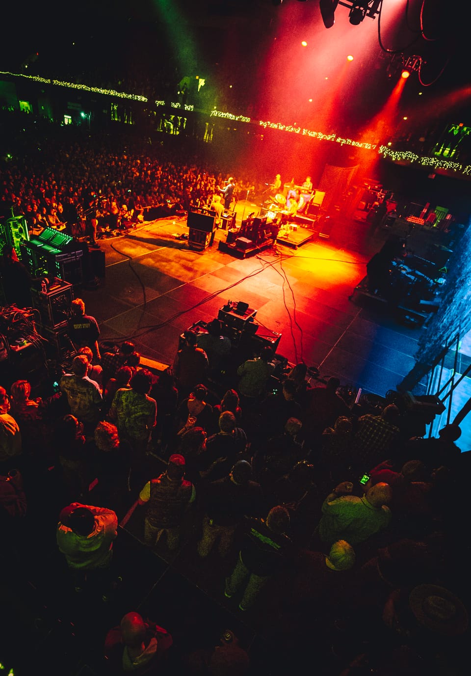 Tyler Childers. A high, wide view of a crowd and a stage lit with red, green and orange beams.