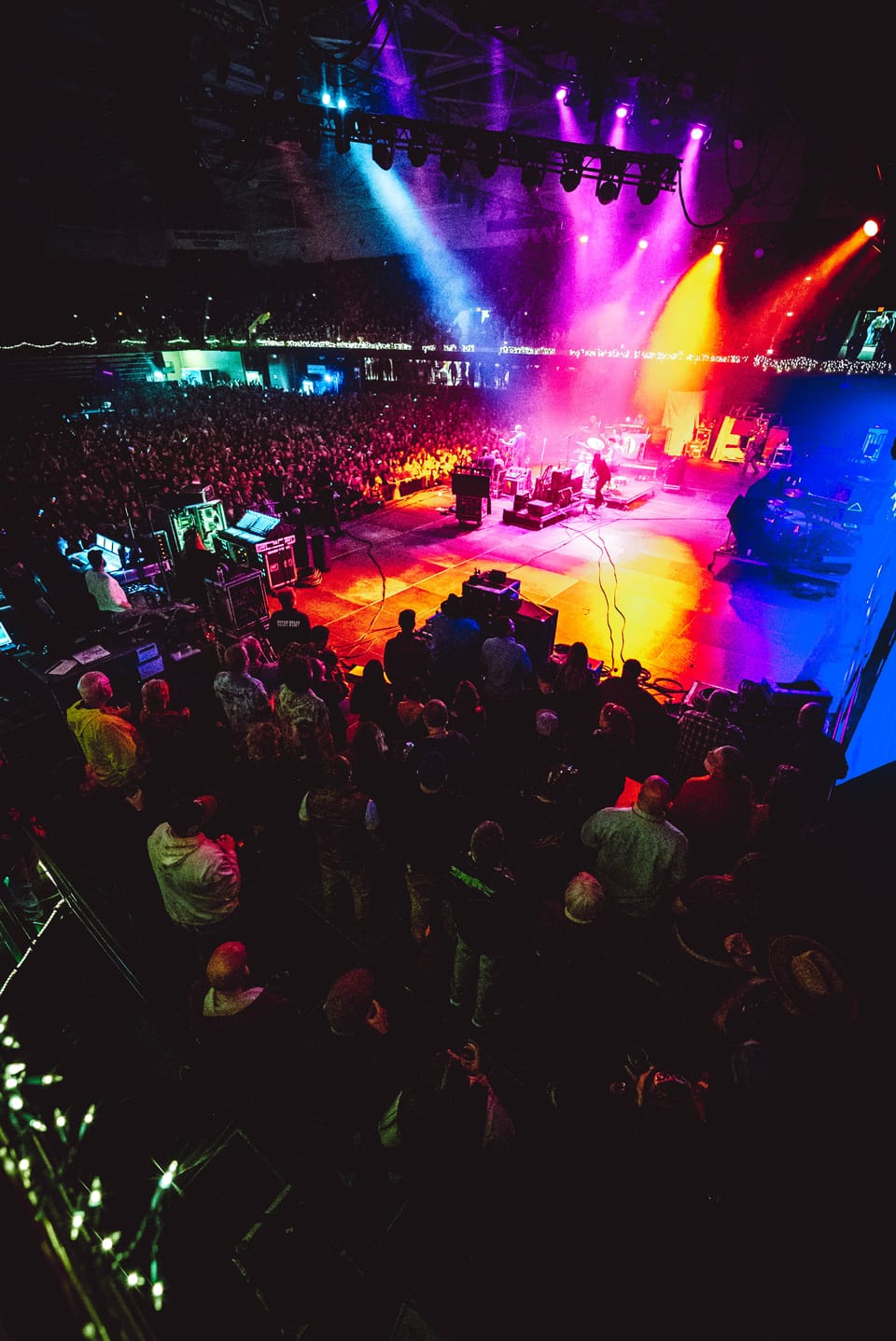 Warren Haynes. A festival crowd faces a stage lit in magenta, orange and blue beams.