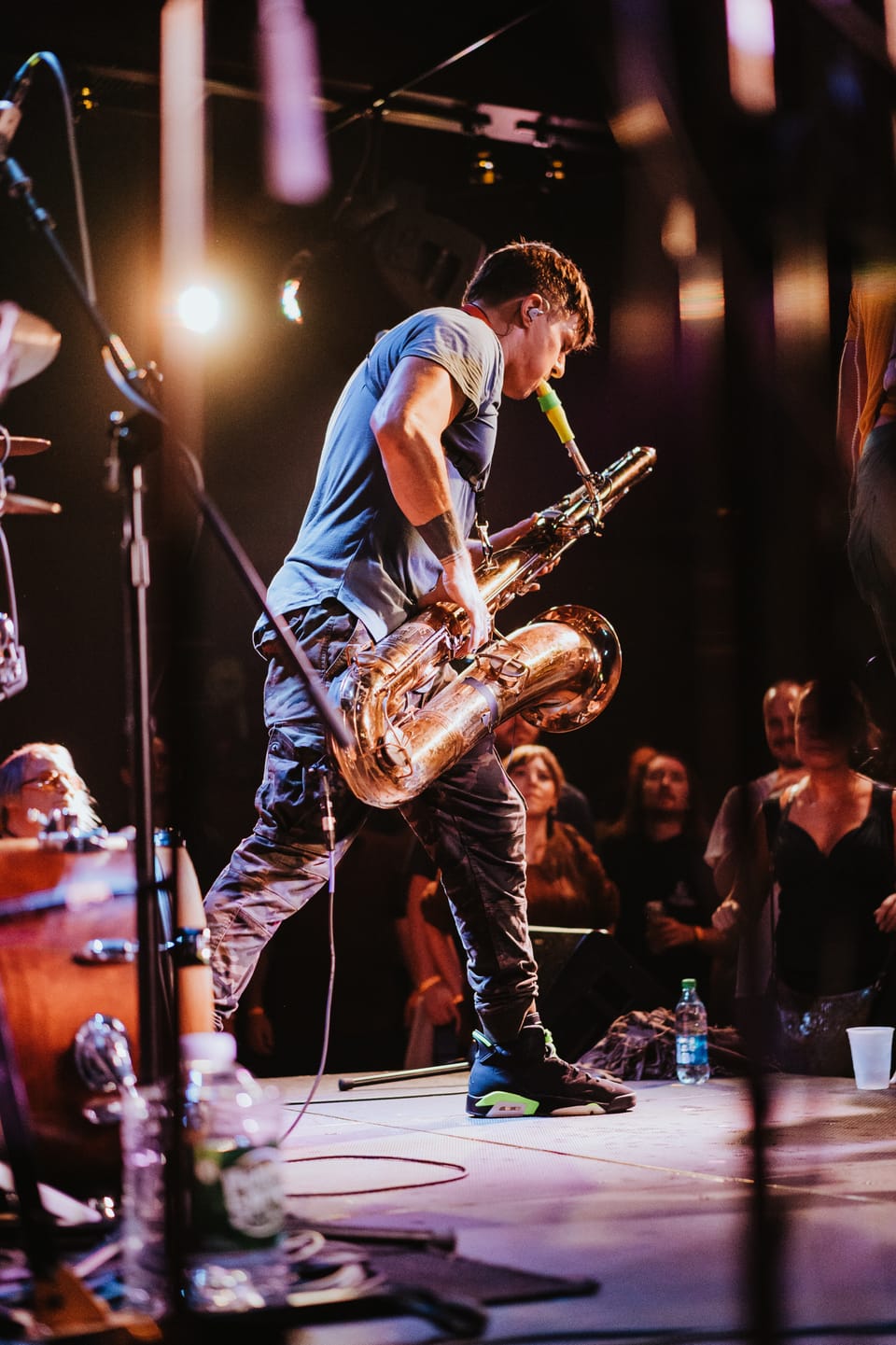 Moon Hooch. A musician plays a large brass horn on a dark stage with a glowing floor.