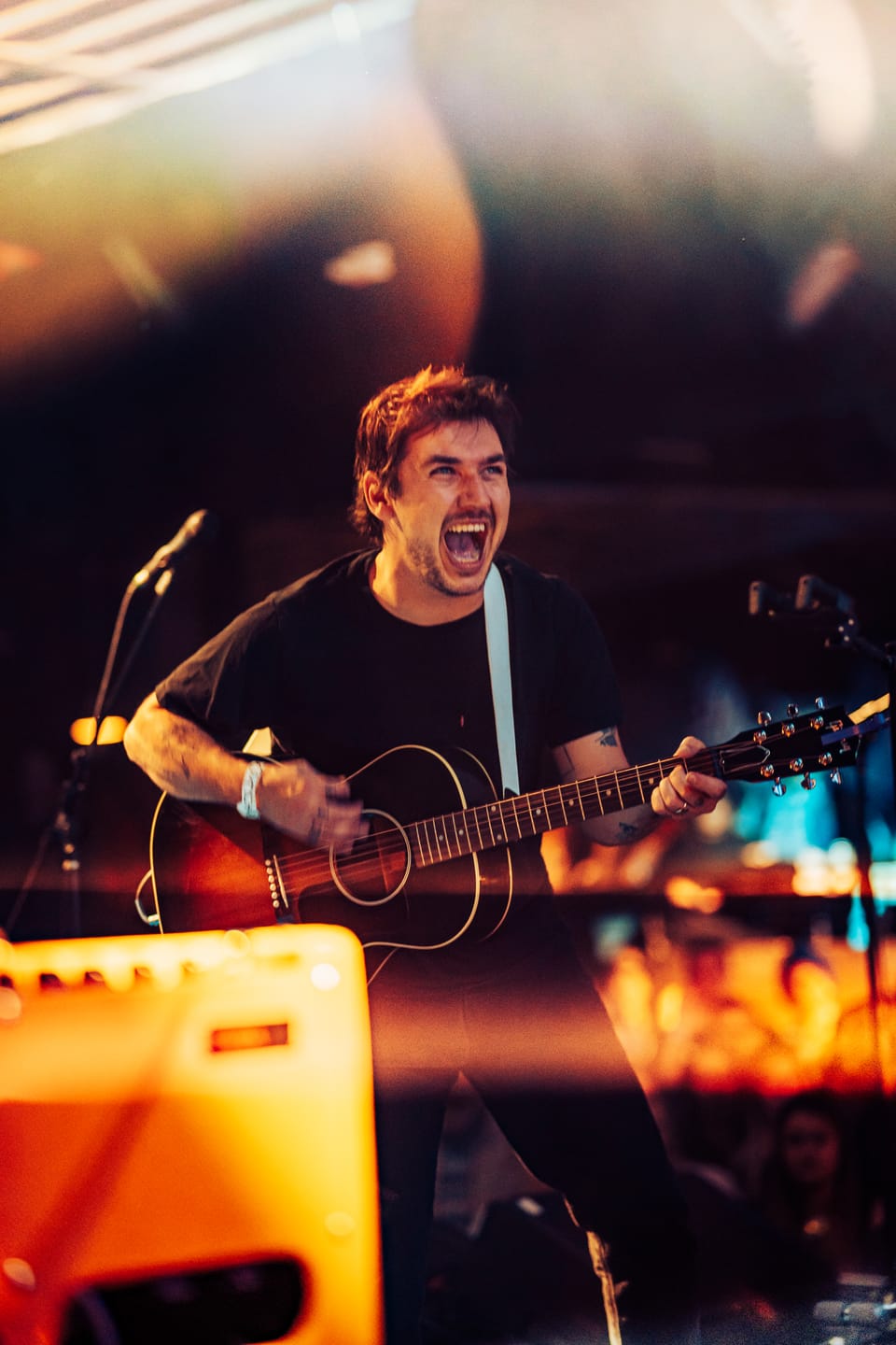 Susto. A singer-guitarist mid-shout plays an acoustic guitar beside an orange amp.