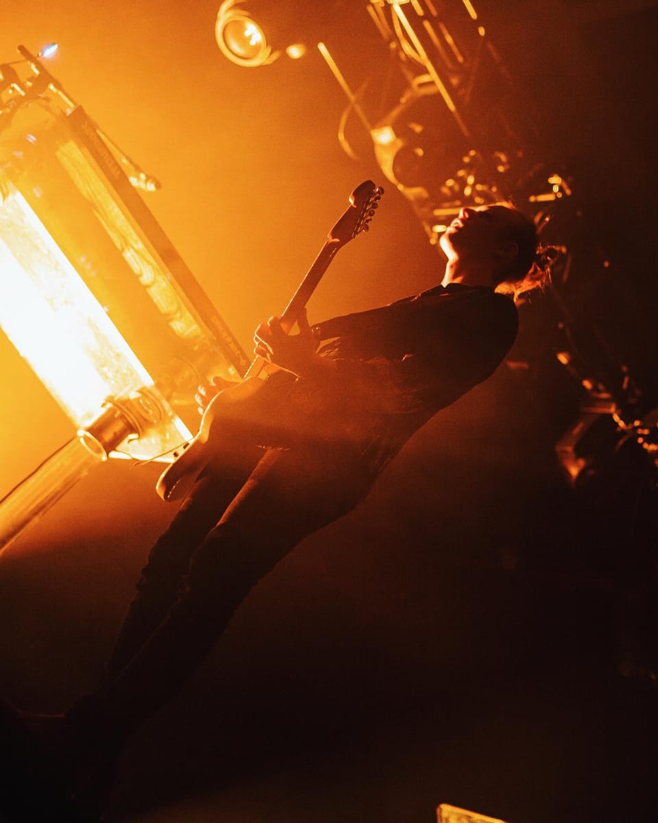 Rufus Du Sol. A guitarist in silhouette leans back toward a glaring orange light.