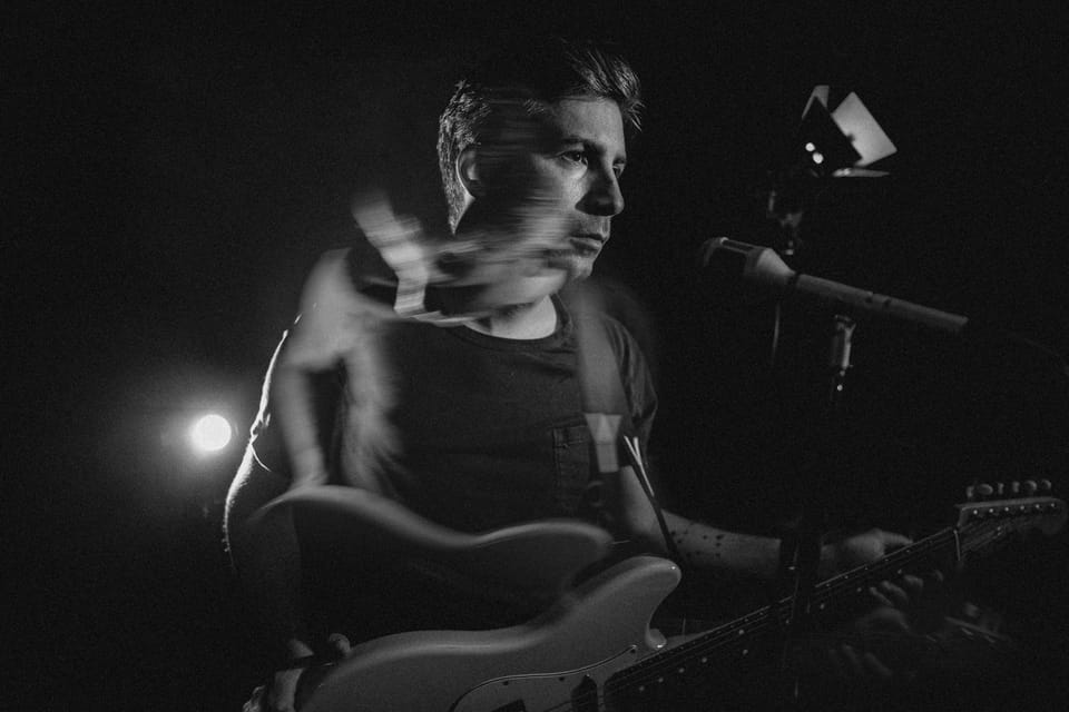 Young Mister. Black and white photo of a singer-guitarist at a microphone, softened by motion blur.