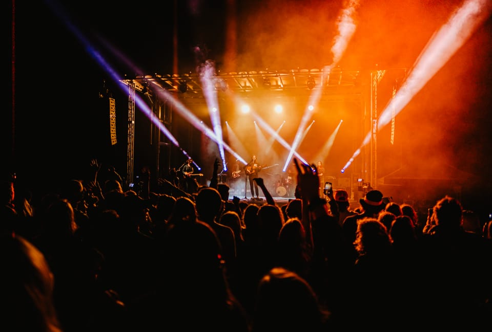 A crowd faces a stage lit with orange smoke and white beams.