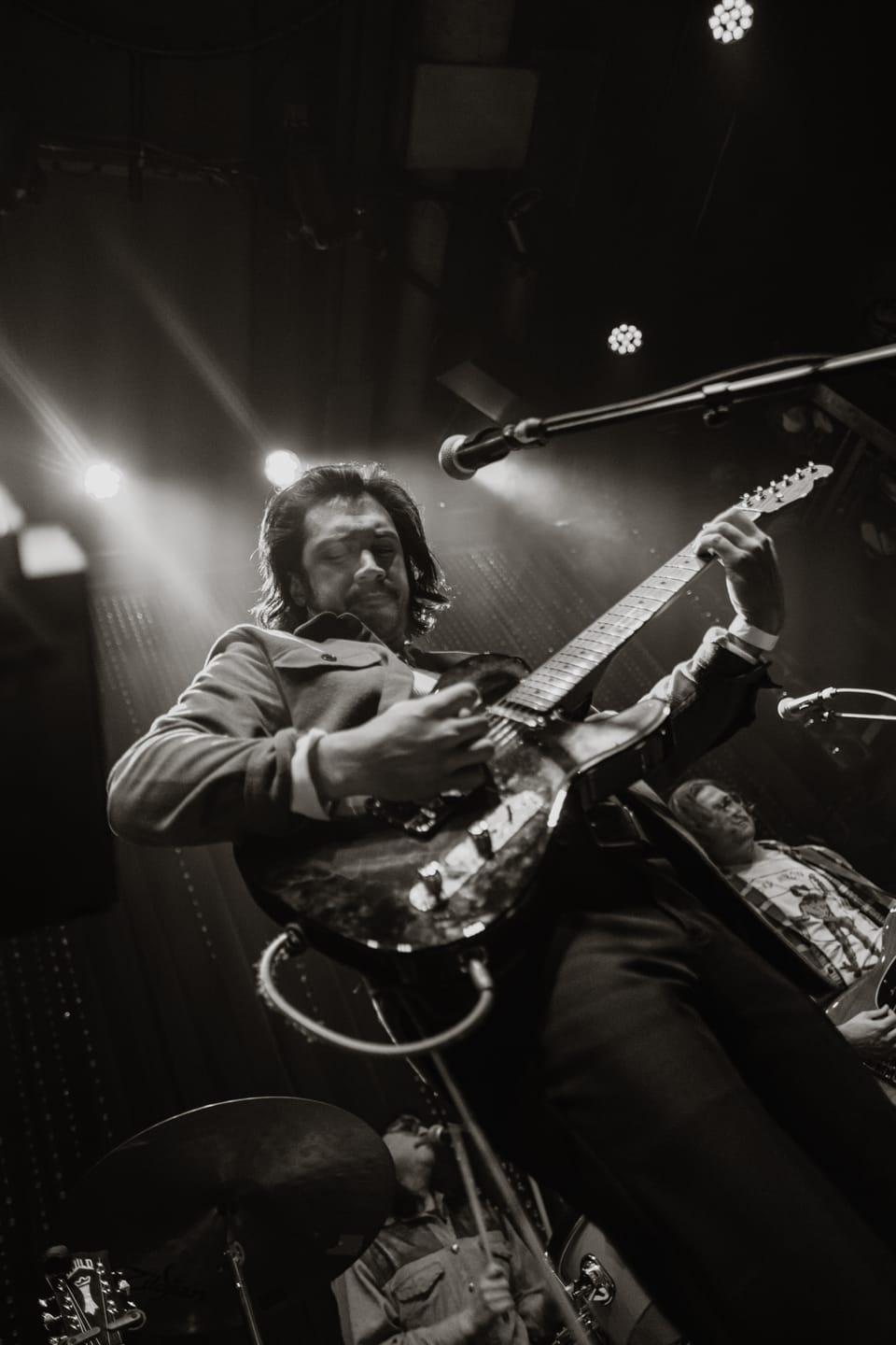 Mo Lowda and the Humble. A black and white shot from below of a guitarist playing, a microphone above him.