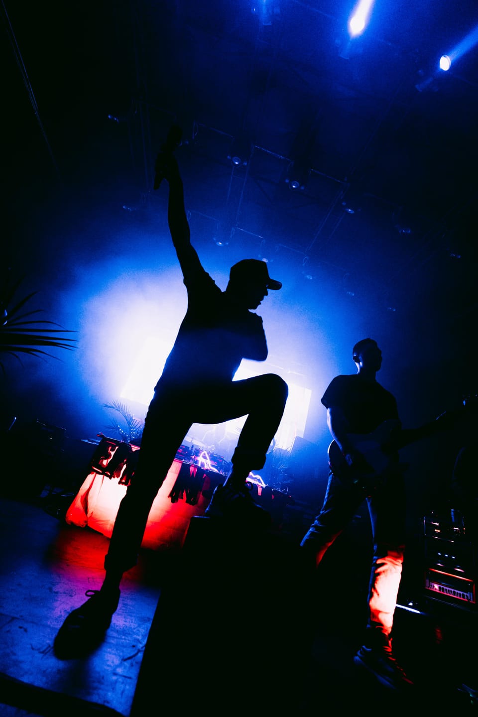 A figure in silhouette leaps with one arm raised against a blue spotlight.