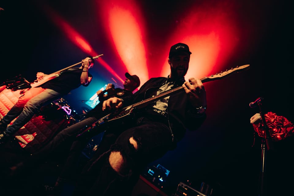 Musicians crowd a stage in a low-angle shot, red lights fanning out behind them.