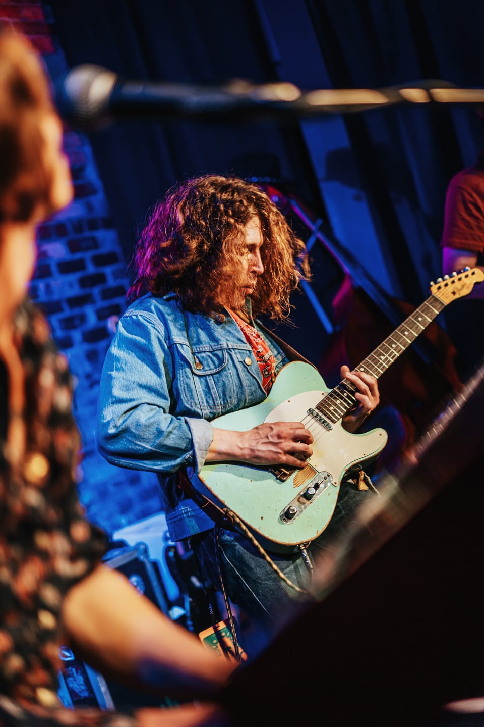 Daniel Donato. A curly-haired guitarist in a denim jacket plays a white Telecaster in front of a blue brick wall.