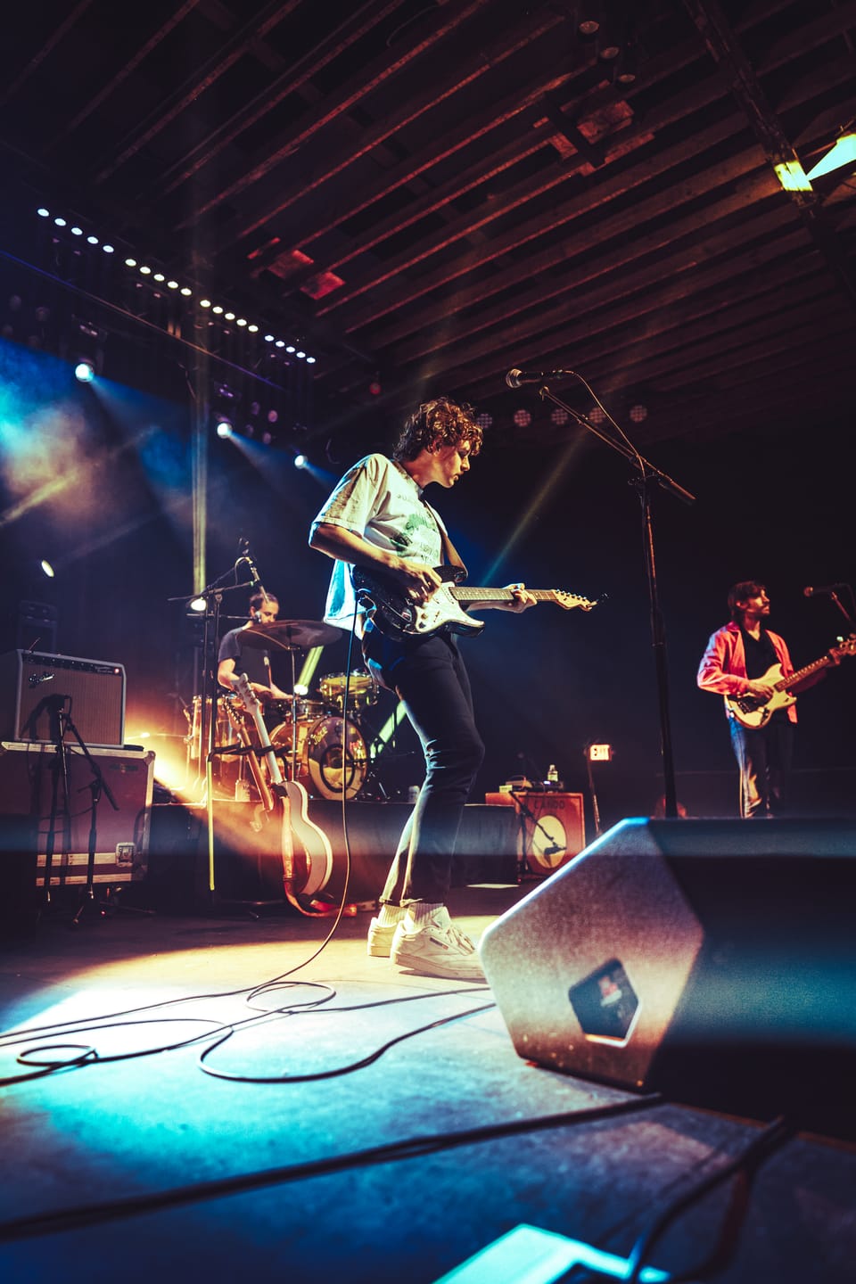 Houndmouth. A guitarist leaps on a smoky stage, with a floor monitor and string lights overhead.