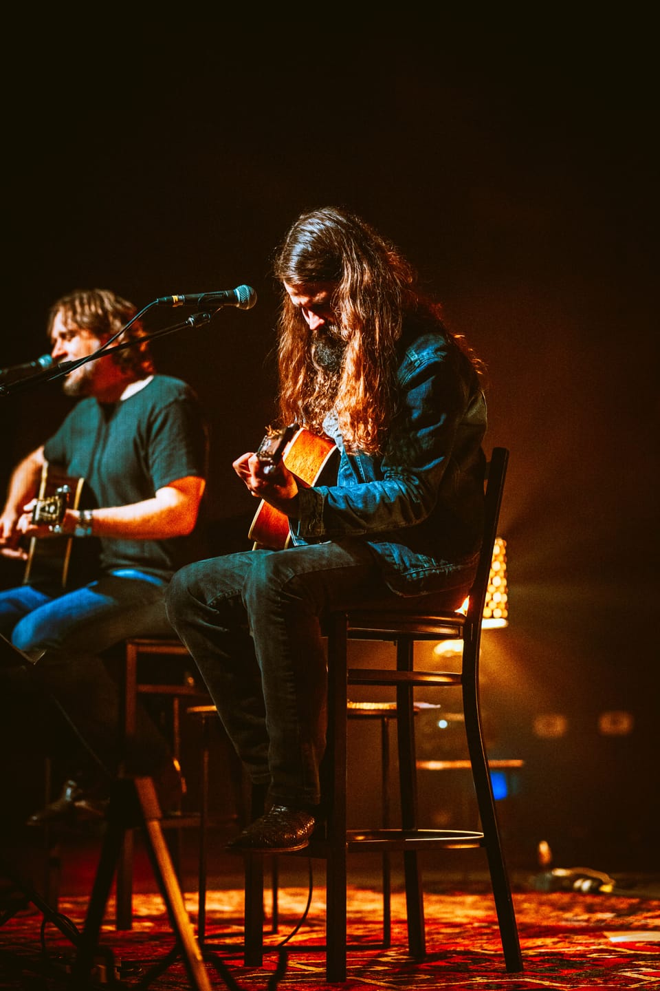Brent Cobb. Two seated acoustic guitarists share a stage on stools, lit warm amber, microphones in front.