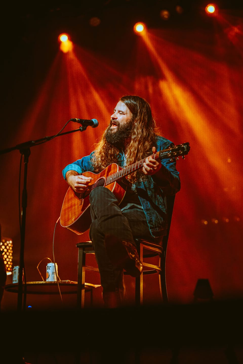 Brent Cobb. A bearded musician sits on a stool playing acoustic guitar under red and orange beams.