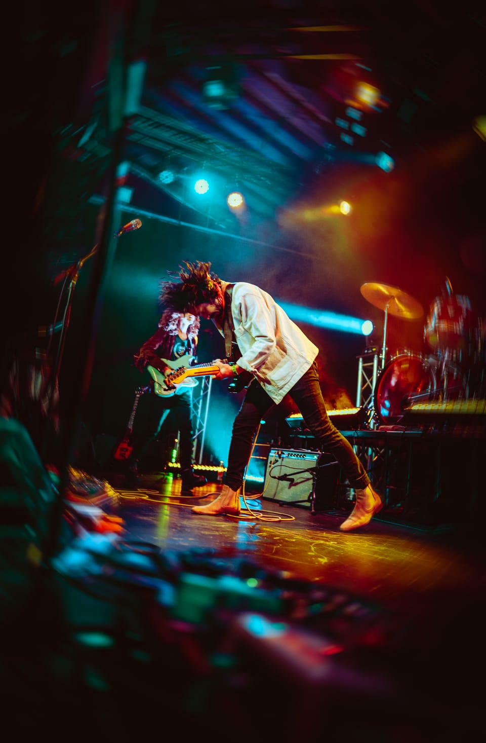 Mo Lowda and the Humble. A guitarist bends low on a stage glowing teal and orange, shot from a low angle.