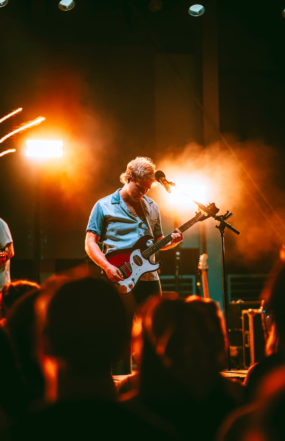 Colony House. A guitarist in a gray shirt plays under glowing orange lights, the crowd in silhouette in front.