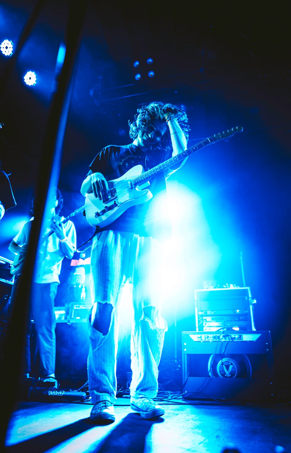 Flipturn. A guitarist stands in a pool of blue light, one hand to his head.
