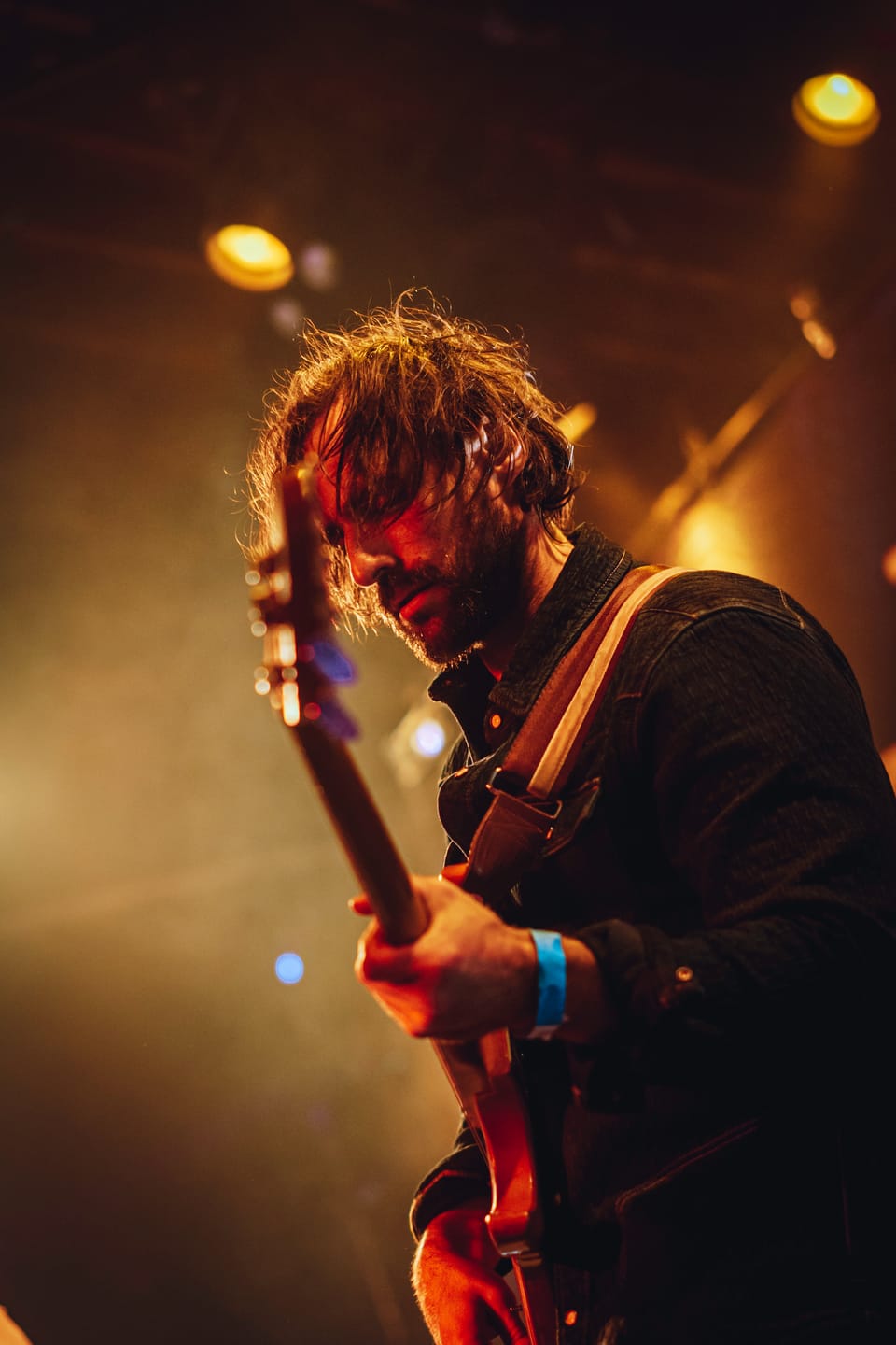 Mo Lowda and the Humble. A guitarist with tousled hair looks down at his strings in warm, hazy light.