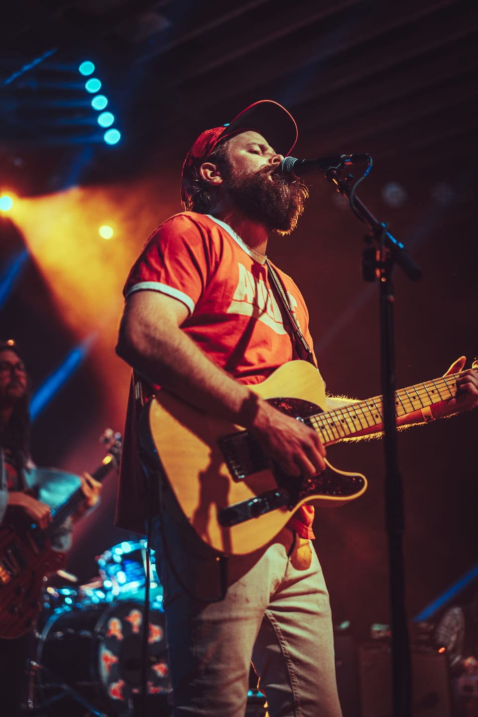 Future Birds. A bearded singer in a red shirt and cap plays an acoustic guitar at a microphone.