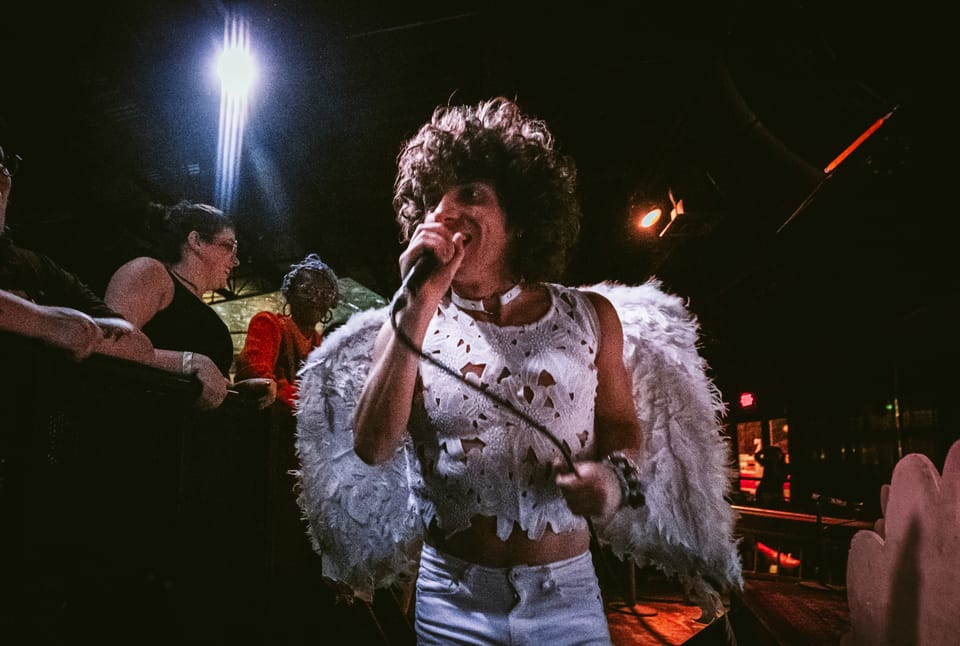 Arlie. A singer in a feathered white jacket sings into a microphone, fans at the stage edge behind.