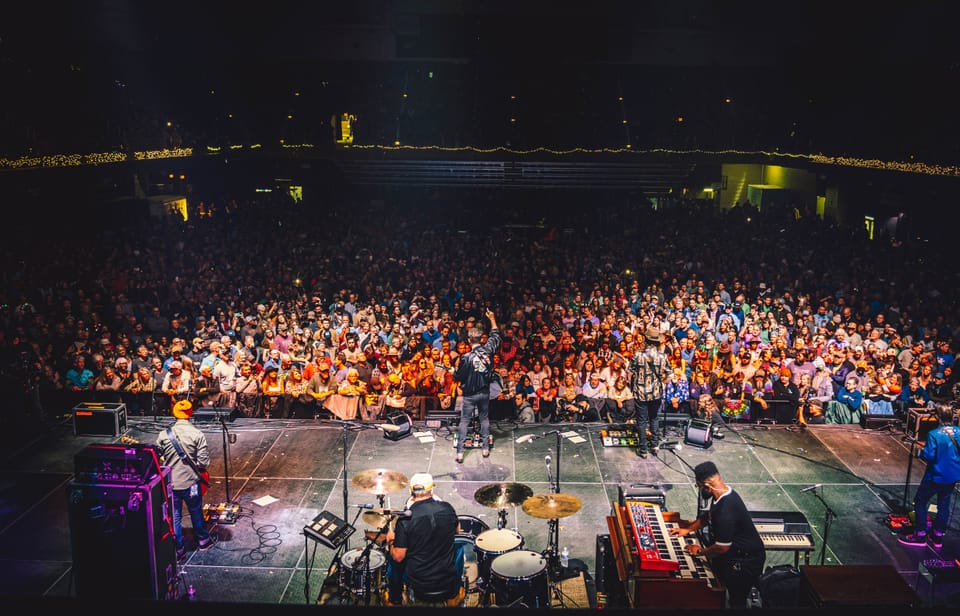 A wide view over a packed, warmly lit crowd, shot from the stage.