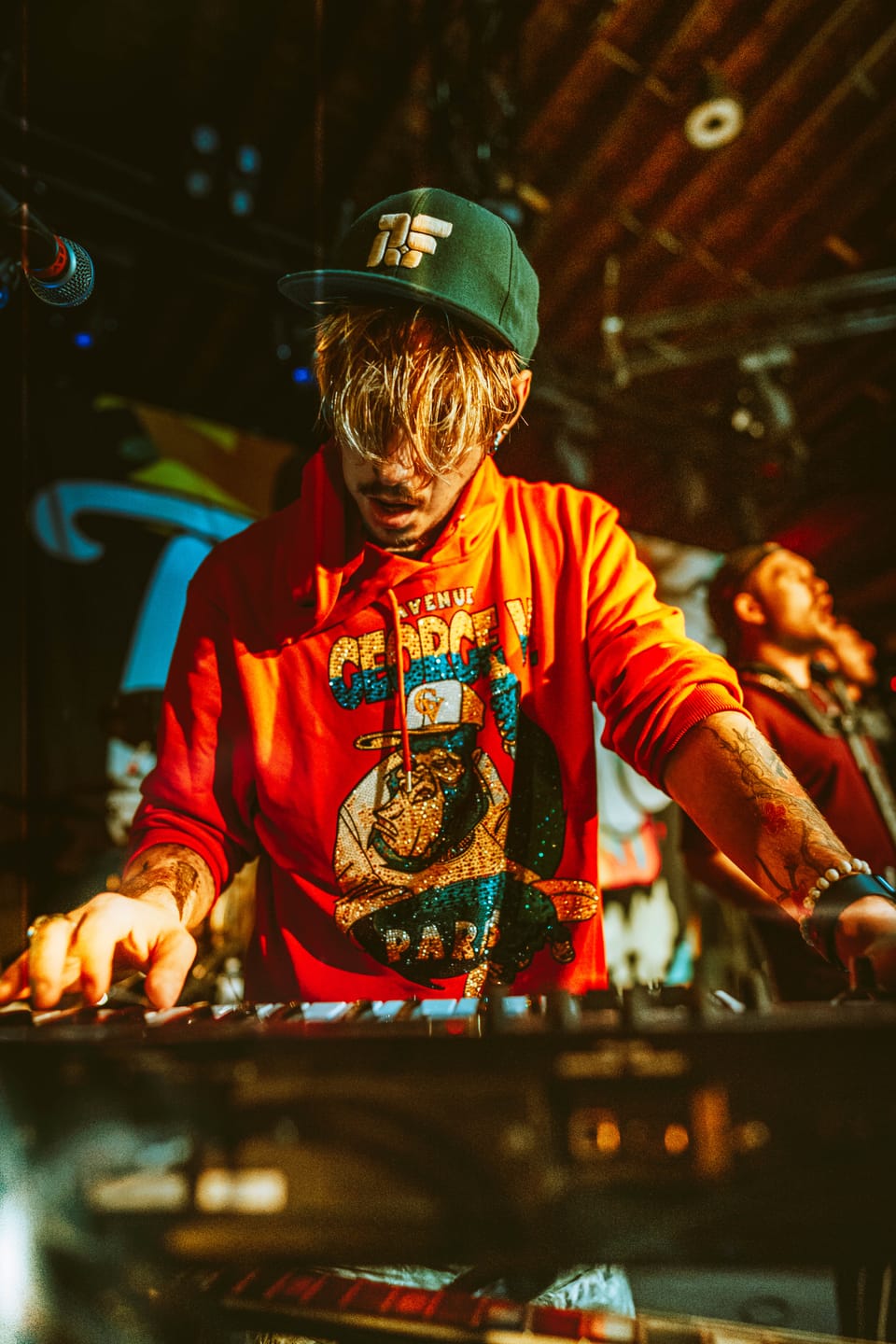Tropidelic. A keyboardist in a red hooded shirt and green cap leans over his keys.