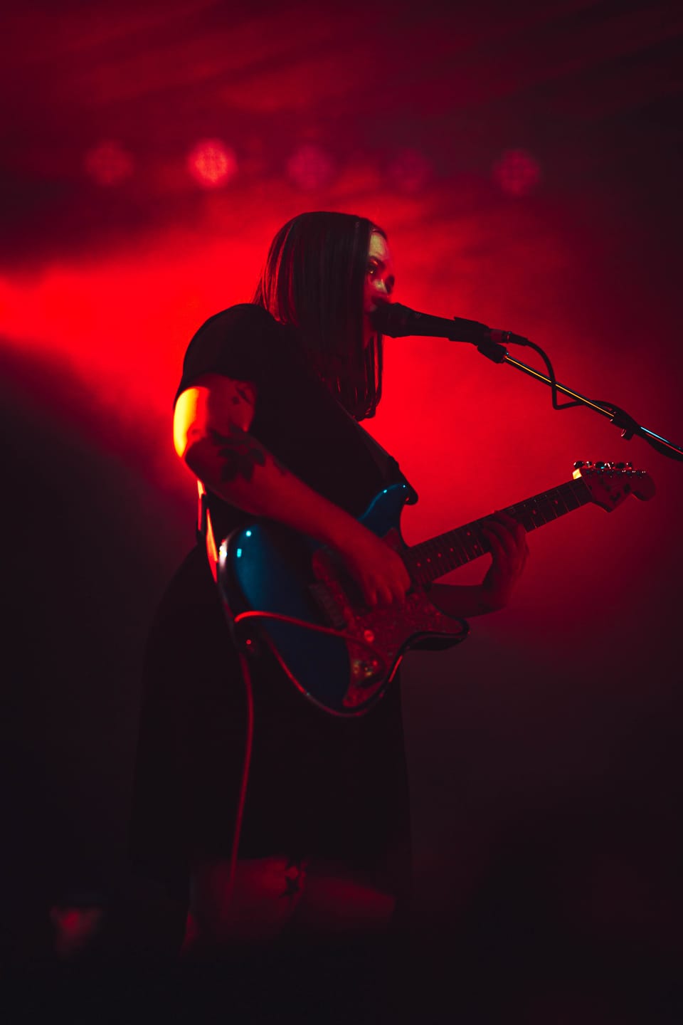 Soccer Mommy. A singer-guitarist glows in saturated red light behind a microphone.