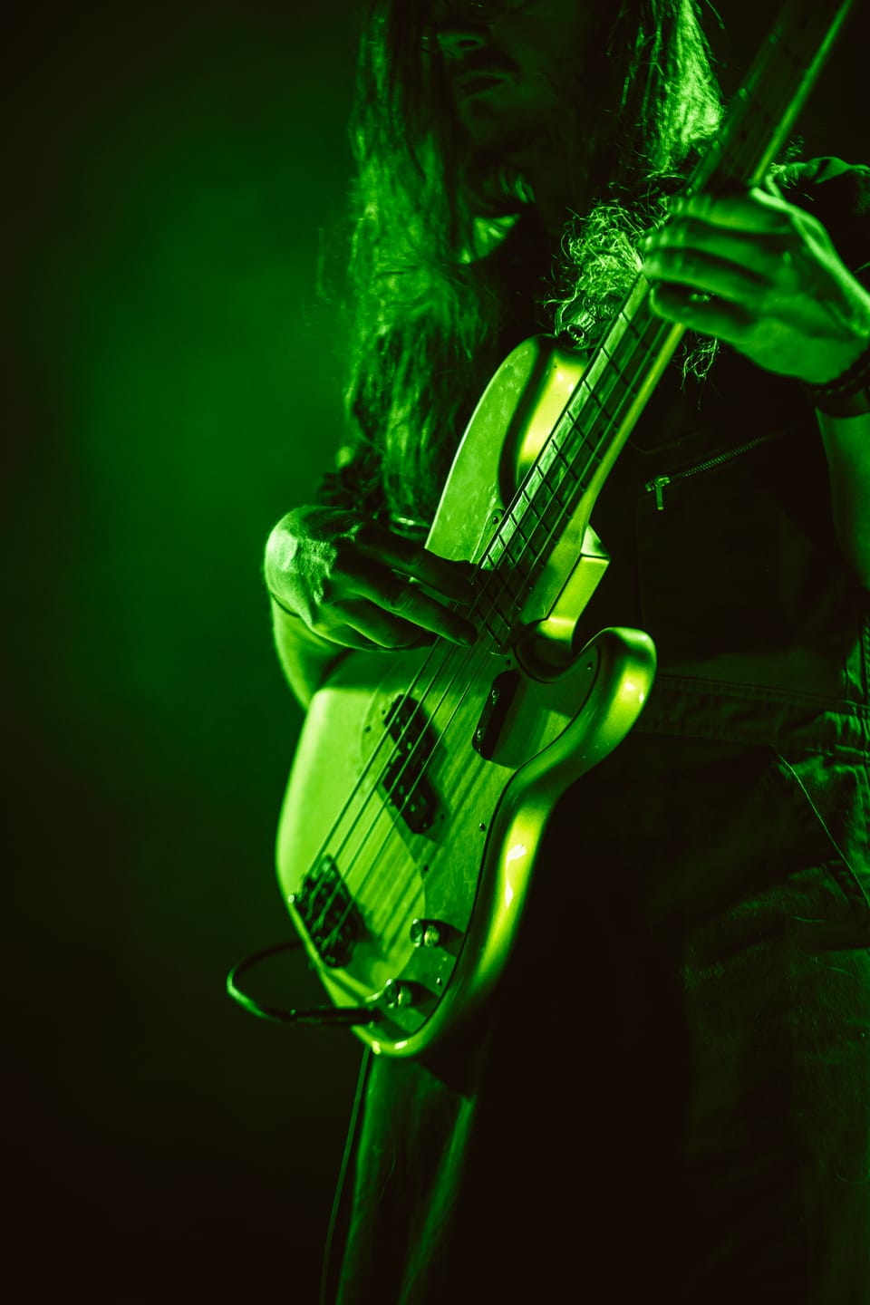 Shakey Graves. A bassist in green light, in a close-up of his hands and the neck of the bass.
